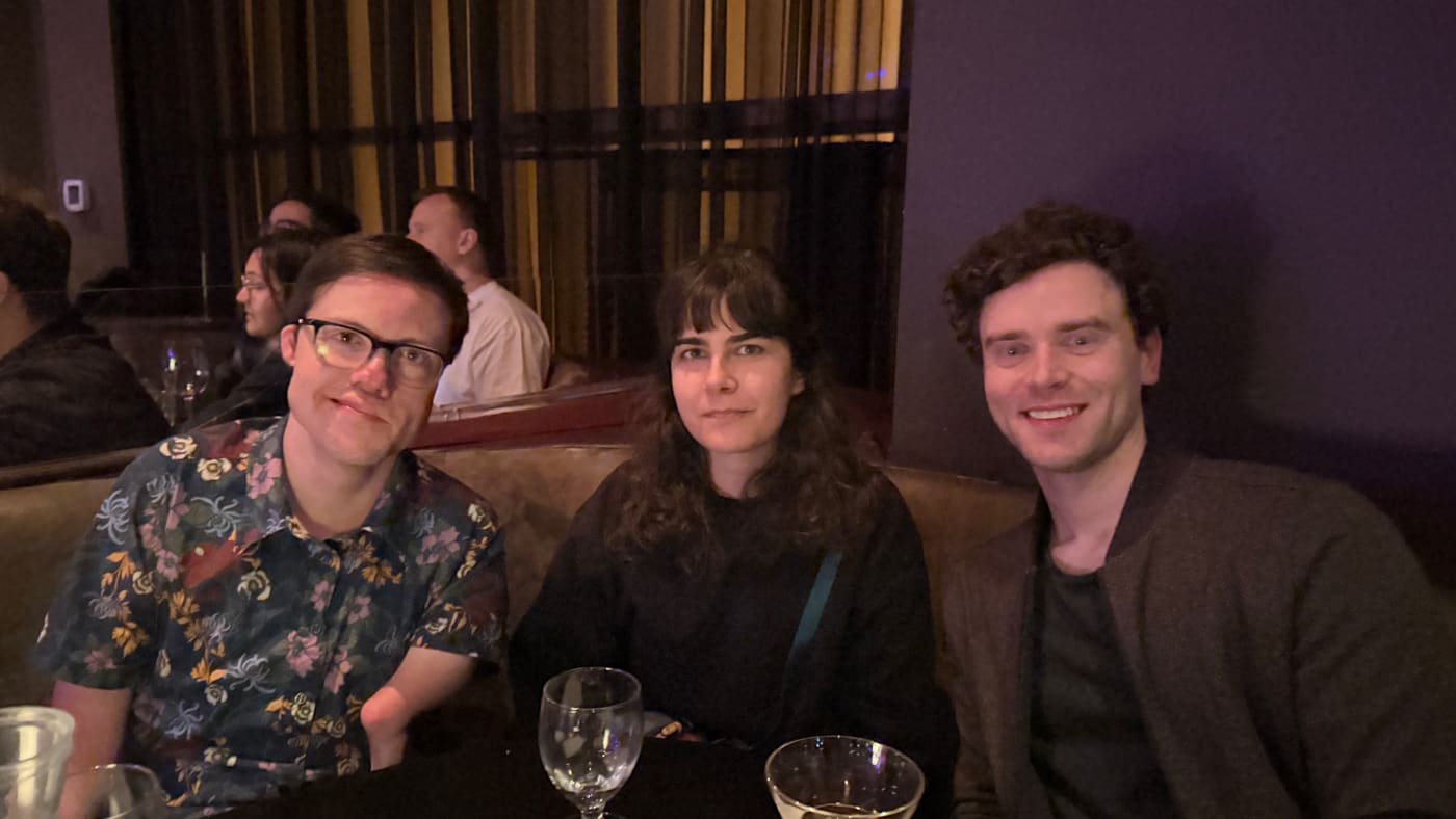 Three coworkers smiling at a dinner table: Gage, Mimi Damnjanovic, and Ben Myers.