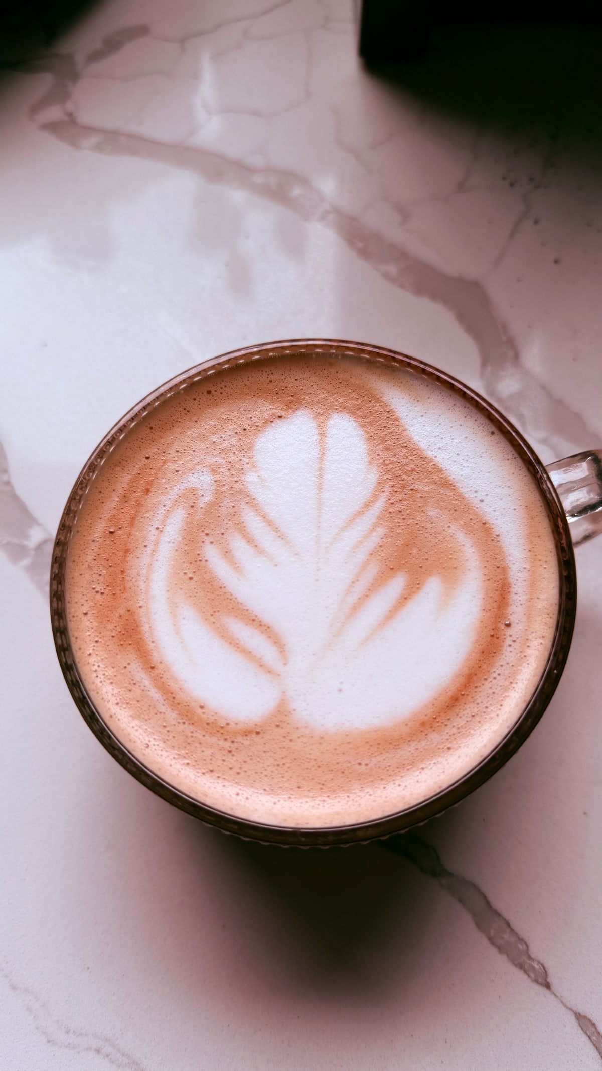 A latte with rosetta latte art, viewed from directly above on a marble countertop.